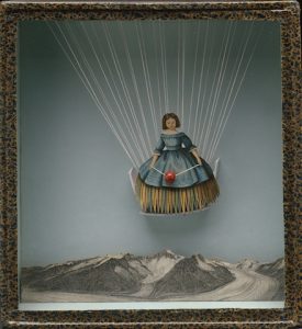a collage in a speckled frame made from paintings of a woman in a blue dress suspended from multiple white threads above a grey landscape of mountains and a glacier