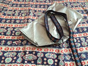 a photograph of blue, white and orange patterned fabric with a bundle of silver tissue paper and decorative ribbon