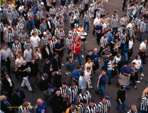 a crowd of football supporters. some are wearing black and white striped shirts